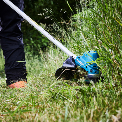 Rasentrimmer in Verwendung, grünem Gras, mit Person in Arbeitskleidung und orangefarbenen Schuhen.