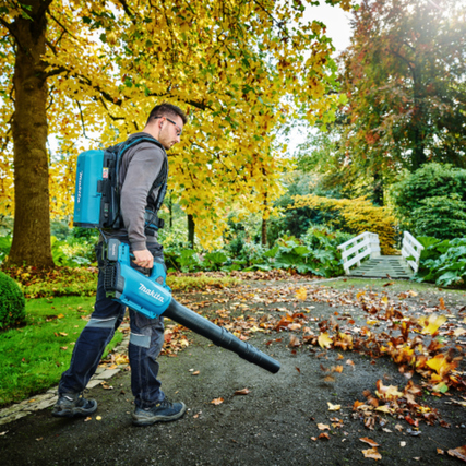 Mann verwendet Laubbläser im Garten, um Blätter auf einem gepflasterten Weg zu entfernen.