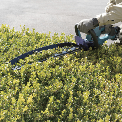 Kabellose Heckenschere in Gebrauch, die über eine Hecke schneidet.