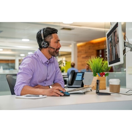 Mann mit Headset arbeitet an einem Schreibtisch mit Monitor, Maus und Kaffee.