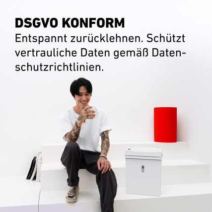 Aktenvernichter in Verwendung, auf einer Treppe neben einer Person und einer roten Dekoration.
