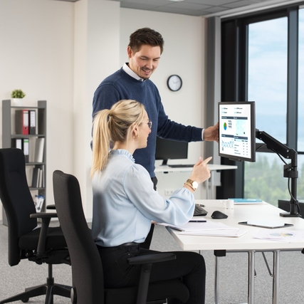 Monitorschwenkarm in einer Büroumgebung mit Personen, die an einem Tisch arbeiten.