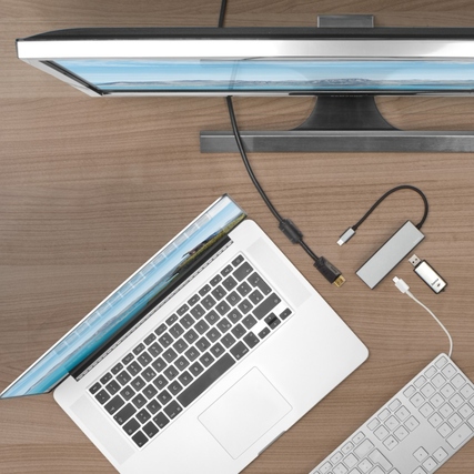 USB-C-Hub mit angeschlossenem Laptop und Monitor auf einem Holztisch.