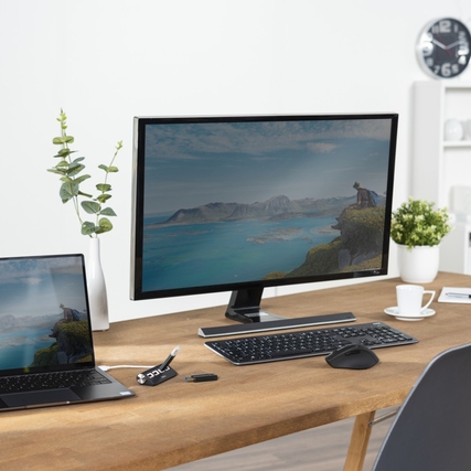 USB-Hub auf einem Schreibtisch zwischen Laptop und Monitor in einem modernen Büroambiente.