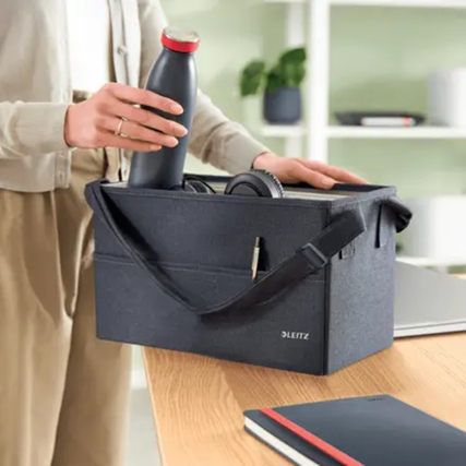 Schwarze Aufbewahrungstasche mit Trinkflasche, Kopfhörern und Notizbuch auf einem Tisch.