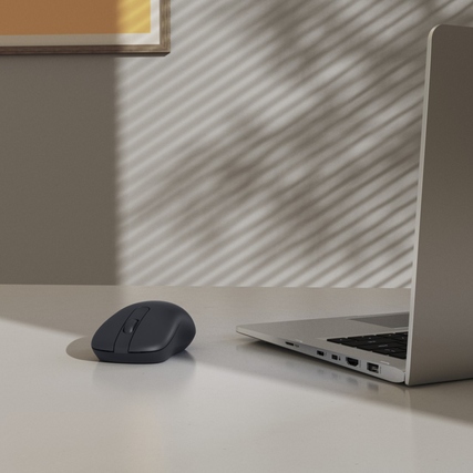 Optische PC-Maus in symmetrischer Form auf einem Tisch neben einem Laptop.