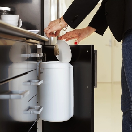 Eine Person entleert einen weißen Müllbeutel in einen integrierten Küchenmülleimer.