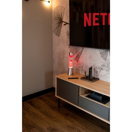 Pinkfarbene Lavalampe auf einem Sideboard mit Fernseher im Hintergrund.