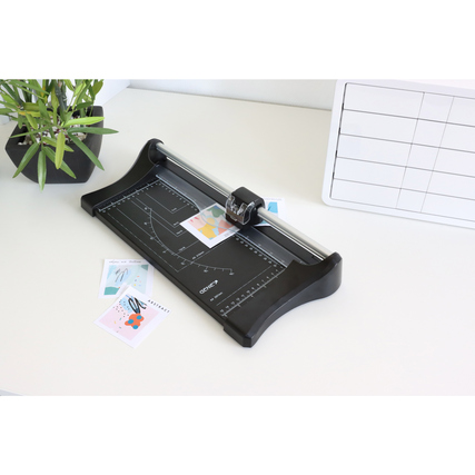 Rollenschneider auf einem Tisch mit Papierstücken und Pflanzen im Hintergrund.