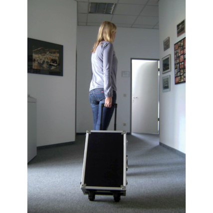 Frau zieht einen Moderationskoffer in einem Büroraum mit grauem Teppich und weißen Wänden.