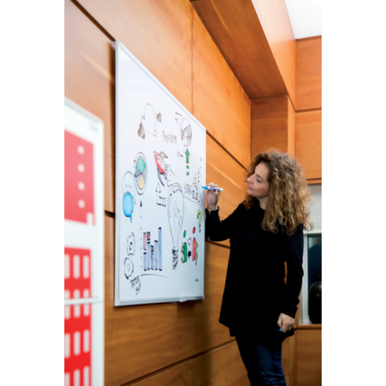 Person schreibt mit einem Marker auf einem großen Whiteboard an einer Holzwand.