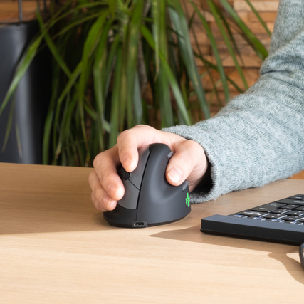 Ergonomische vertikale PC-Maus in Verwendung, Hand greift die Maus, Tischumgebung im Hintergrund.