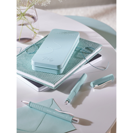 Lichtblaues Schreibgeräteset mit Füller, Kugelschreiber und Notizbuch auf einem Tisch.