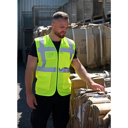 Gelbe Warnweste mit Reflexstreifen, getragen von einer Person in einem Lagerumfeld.