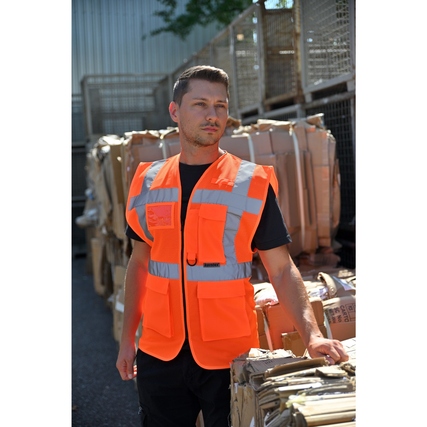 Person trägt eine signal-orange Warnweste mit Reflexstreifen vor einem Lagerhintergrund.