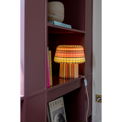 Papierleuchte in buntem Design steht auf einem Regal zwischen Büchern und einer Vase.