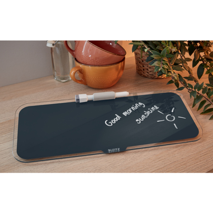 Graues Memoboard auf einem Tisch mit einer dekorativen Pflanze und Tassen im Hintergrund.