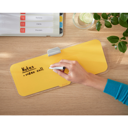 Gelbes Memoboard mit handschriftlichen Notizen, auf einem Tisch mit Pflanzen und Ablage.