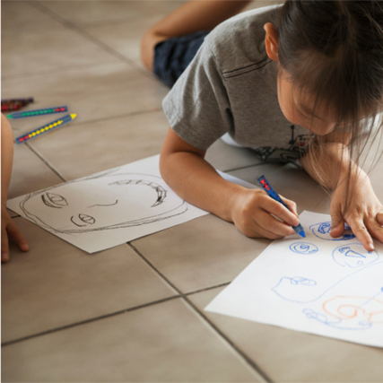 Kind malt mit Wachsmalstiften auf Papier, während ein weiteres Bild neben ihm liegt.