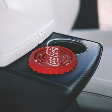 Lufterfrischer im Design eines Coca-Cola-Flaschenverschlusses auf einem Fahrzeuginnenraum.