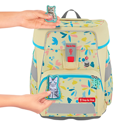 Hände halten wechselbare Anhänger für einen Schulranzen mit buntem Muster und Magnetflächen.