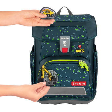 Hand, die ein Magnet-Zubehörteil an einen Schulranzen mit bunten Applikationen anbringt.