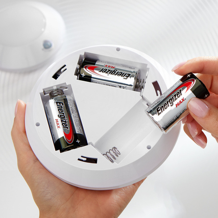 Eine Hand setzt eine Energizer Max D-Batterie in ein weißes Batteriefach eines Geräts ein.