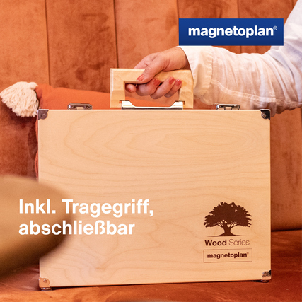 Holzkoffer mit Tragegriff und Gravur, auf einer Couch abgestellt.