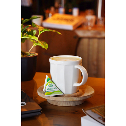 Tasse mit Getränk auf einem Holzuntersetzer, daneben ein Mini Tetraeder Milch.