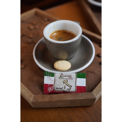 Biscotti in einer Verpackung neben einer Tasse Kaffee auf einem Holztablett.