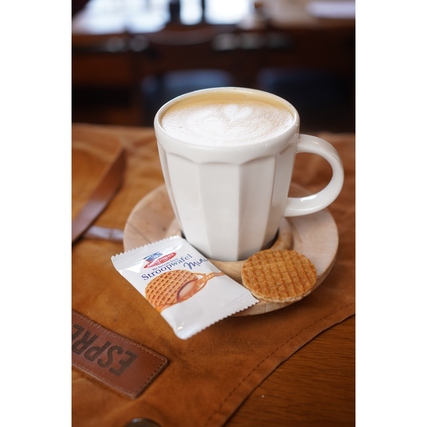 Stroopwafel Mini neben einer Tasse Kaffee auf einer Unterlage, , mit Verpackung und Keks sichtbar.