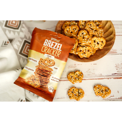 Packung Brezel Cracker Sesam neben einer Schüssel mit Cracker auf einem dekorativen Untergrund.