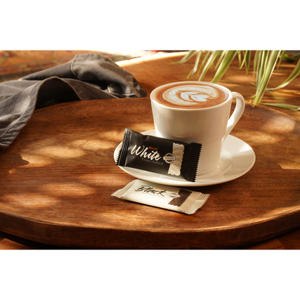 Zwei Kekspackungen in schwarz und weiß liegen auf einem Holztisch neben einer Tasse Kaffee.
