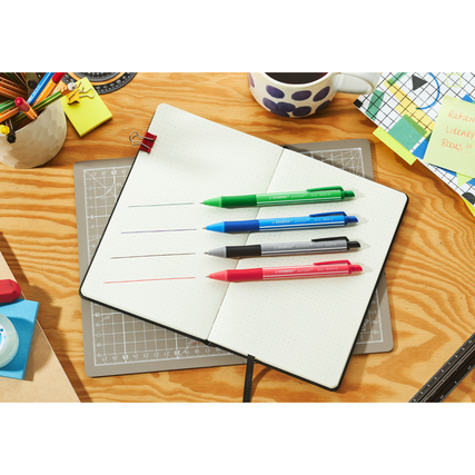 Kugelschreiber in verschiedenen Farben liegen auf einem offenen Notizbuch und einer Holzoberfläche.