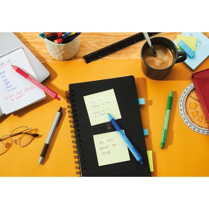 Kugelschreiber in verschiedenen Farben auf einem Tisch mit Notizblock und Kaffeetasse.