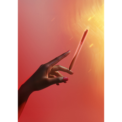 Hand mit Kugelschreiber vor einem farbigen, lichtdurchfluteten Hintergrund.