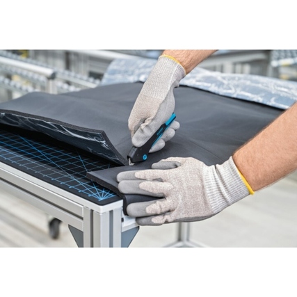 Ein Handwerker mit Arbeitshandschuhen schneidet mit einem Sicherheitsmesser über einem Tisch.