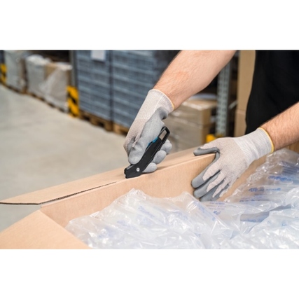 Hand mit grauen Arbeitshandschuhen schneidet eine Kartonschachtel mit einem Sicherheitsmesser auf.