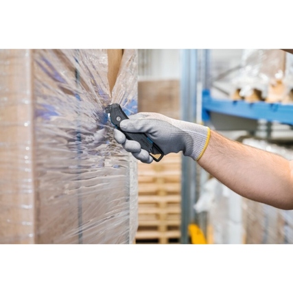 Ein Hand mit einem grauen Arbeitshandschuh hält ein Sicherheitsmesser, das durch Folie schneidet.