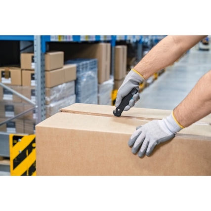 Hand mit grauen Handschuhen, die ein Sicherheitsmesser an einer Kartonschachtel verwendet.