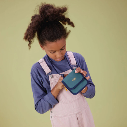 Brustbeutel in Hand eines Kindes, fröhlich und im Gebrauch, mit grün-blauem Design.