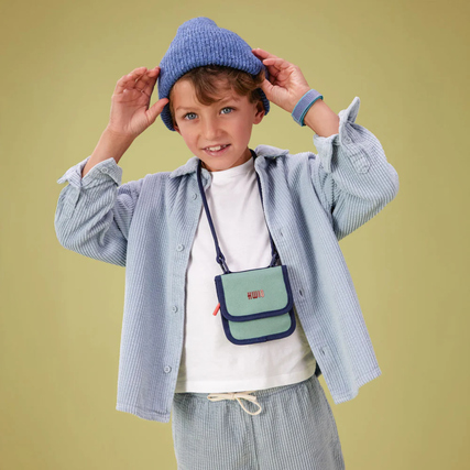 Brustbeutel in Grünen und Blau, getragen von einem Kind, steht vor einfarbigem Hintergrund.