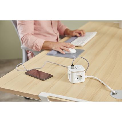 Kompakter Steckdosenwürfel mit mehreren Anschlüssen auf einem Tisch, daneben ein Smartphone.