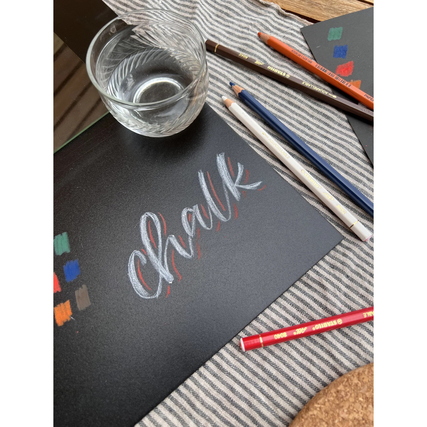 Buntstifte auf einem Tisch mit einem Glas und einer Kreideinschrift auf schwarzem Papier.