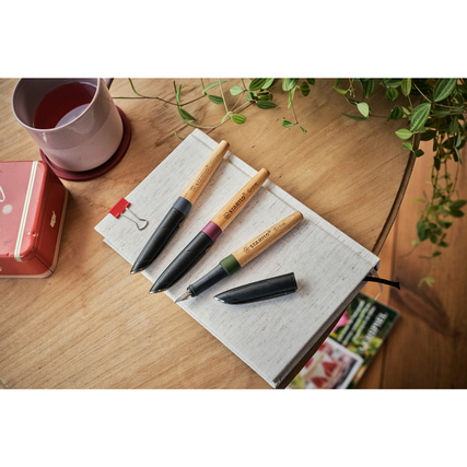 Füllfederhalter in verschiedenen Farben auf einem Notizbuch und Tisch, dekorativ arrangiert.