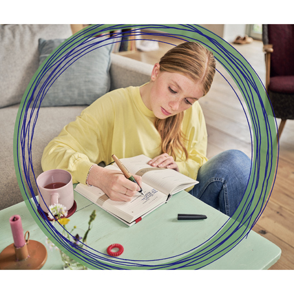 Füllfederhalter in Nutzung, auf einem Tisch neben einem Getränk und Schreibmaterialien.