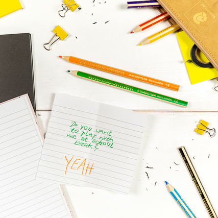 Buntstifte in verschiedenen Farben liegen auf einem Tisch neben Notizblöcken und Büroklammern.