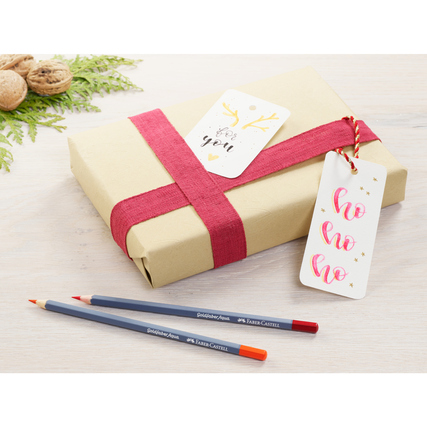 Geschenkverpackung mit roten Bändern und Tags, daneben zwei Faber-Castell Aquarellstifte.
