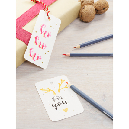 Faber-Castell Aquarellstifte liegen neben dekorierten Geschenkanhängern auf einem Tisch.