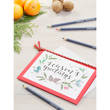 Aquarellstifte liegen neben einer Grußkarte und Dekoration auf einem Tisch.